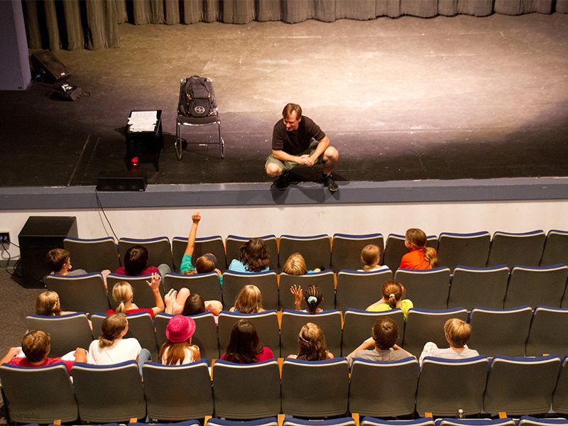 An audience of students watches a performer on the CTA stage