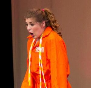 A surprised performer in an orange jumpsuit on stage