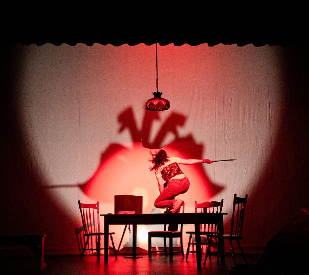 A performer leaps over a table in a dramatic red-lit scene from She Kills Monsters (2020-21)