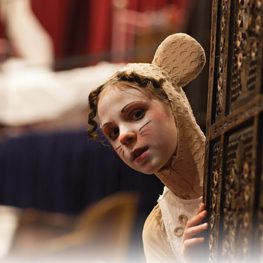 A young performer in a mouse costume peeks around a doorway on stage